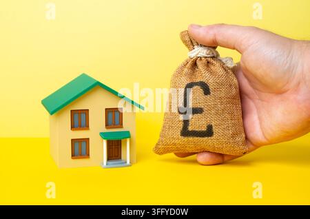 Ein Wohngebäude und eine Hand, die einen Geldbeutel mit britischen Pfund hält. Hauskauf, Investitionen in Immobilien. Trends auf dem Wohnungsmarkt. Sanierung von Wohngebäuden Stockfoto