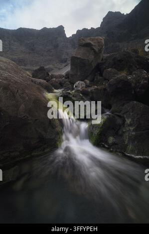 Bergbach stürzt über moosbewachsene Felsbrocken unter den schroffen Cuillin-Gipfeln auf der Insel Skye, Schottland. Stockfoto