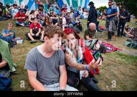 PAAR, DAS EIN SELFIE IN EINER FESTIVALSCHARENDE NIMMEN, REPORTAGE, GREEN MAN FESTIVAL 2015, BRECON, WALES, UK, 2015: Eine junge Frau mit roten Dreadlocks und einem Tattoo macht ein Selfie mit ihrem männlichen Freund, während sie auf dem Gras inmitten einer großen Festivalmenge sitzen. Foto: Rob Watkins. INFO: Das Green Man Festival findet jährlich im August in den Brecon Beacons statt. Es feiert alternative Musik, Kunst, Literatur, Wissenschaft und familienfreundliche Kultur in einer wunderschönen Berglandschaft. Die Veranstaltung 2015 begann sonnig, wurde aber durch nächtlichen Regen an den letzten beiden Tagen schlammig. Stockfoto