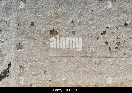 Alte verwitterte Wand mit abblätternder weißer Farbe und Rissen. Grunge-Betonhintergrund mit beschädigtem Putz und freiliegender grauer Steintextur. Stockfoto