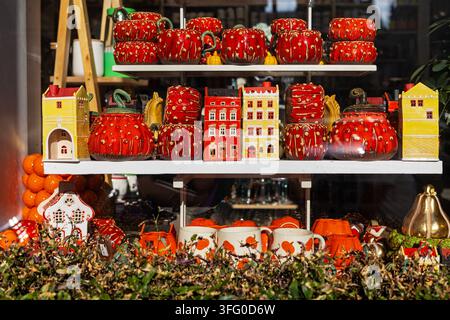 Herbst-Schaufenster mit roter Keramik und Miniaturhäusern. Herbstschaufenster mit roten Keramik-Kürbissen, Miniaturhäusern, Tassen, orangefarbenem Dekor und Stockfoto