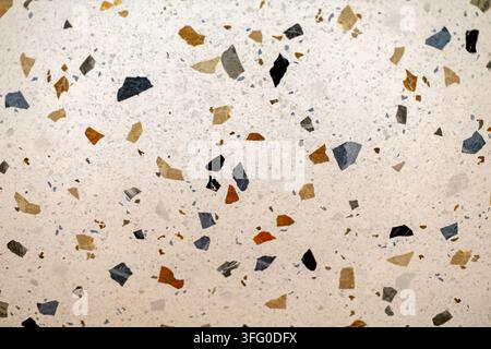 Weiße Terrazzo-Oberfläche mit mehrfarbigen Steinspänen. Nahaufnahme von weißem Terrazzo mit verstreuten blauen, schwarzen, grauen, hellbraunen und orangefarbenen Steinspänen. Stockfoto