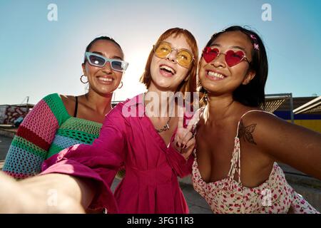 Drei glückliche, vielfältige junge Frauenfreundinnen, die in die Kamera lächeln, ein Selfie machen und auf einem sonnigen Tag Freundschaft und Jugend feiern Stockfoto