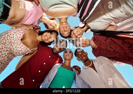 Gruppe glücklicher, vielfältiger junger Erwachsener, die lächeln, Freundschaft und Gemeinschaft umarmen, zusammen in einem Kreis stehend, Blick von unten Stockfoto