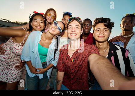Fröhliche, vielfältige junge Freunde lächeln und schauen in die Kamera, während sie zusammen im Sommer im Freien ein Selfie machen Stockfoto