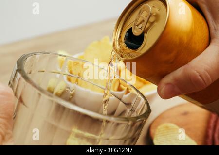 Dosenbier, das in einen Krug gegossen wird. Hand, die ein Bier aus der Dose in einen Bierkrug gießt. Frauenhand hält eine gelbe Aluminiumdose und gießt Bier. Stockfoto