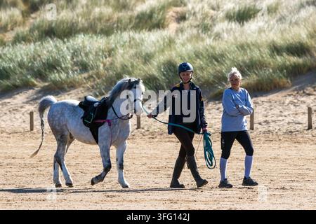 Eine Reiterin führt ein geschecktes graues Pony entlang eines sandigen Strandes in Southport, UK. Stockfoto