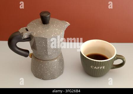 Italienische Moka-Kanne und Kaffeetasse, die als Stillleben auf einem neutralen Hintergrund arrangiert sind Stockfoto