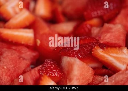Eine extrem nah aufgenommene Fotografie, die ein lebhaftes, rotes Gemisch aus frisch gehackten Wassermelonenstücken und in Scheiben geschnittenen Erdbeeren zeigt, die in einem Obstsalat vermischt sind Stockfoto