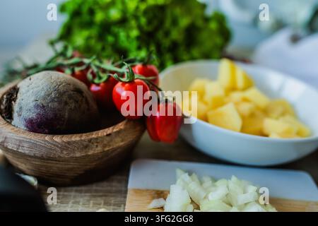 Verschiedene Gemüse- und Obstsorten sind auf einem Küchentisch platziert. Es gibt Tomaten, Zwiebeln, Rüben und gewürfelte Ananas in Schüsseln und auf einem Schneidebrett Stockfoto