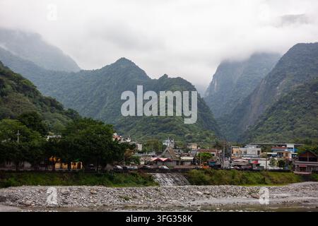 Neblig grüne Berge mit Blick auf das Dorf Sanzhanxi in Hualien, Taiwan. Felsenbett und üppige Vegetation unter einem bewölkten Himmel. Stockfoto