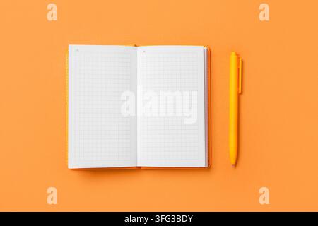 Planung und Produktivität, offenes Rasternotizbuch mit gelbem Stift auf orangefarbenem Hintergrund für kreatives Brainstorming und Zielsetzung im Büro oder in der Schule Stockfoto