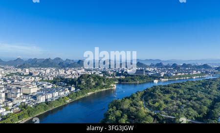 Die sonnenbeschienene Stadt Guilin erstreckt sich am frühen Morgen entlang des Li-Flusses, zentriert um den ikonischen Elefantenrüsselhügel; Karstberge erheben sich in der Ferne unter einem klaren blauen Himmel, China. Stockfoto