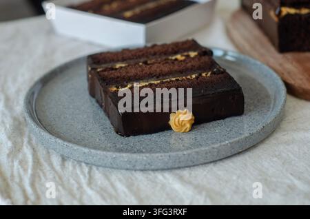 Reicher Schokoladen-London-Kuchen, geschichtet mit Karamell und überzogen mit glänzender Ganache, garniert mit gekniffeltem Zuckerguss Stockfoto
