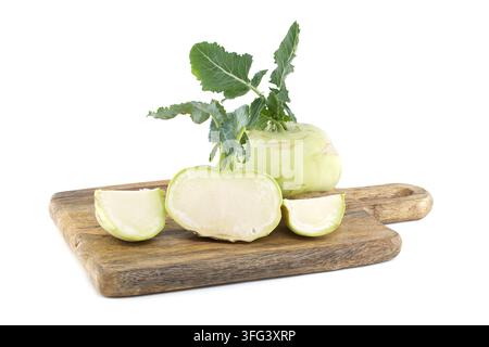 Ganze und geschnittene Kohlrabiknollen mit grünen Blättern, die auf einer strukturierten Holzplatte vor weißem Hintergrund angeordnet sind Stockfoto