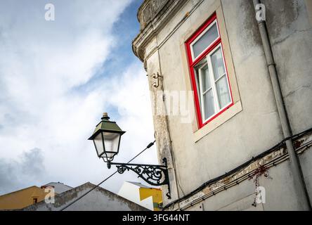 Gusseiserne Straßenlaterne neben einem rotgerahmten Fenster, alte Stadtfassade, Lissabon, Portugal, Vintage-Stadtcharme Stockfoto