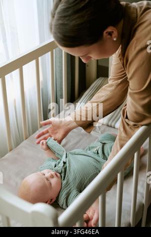 Fürsorgliche Mutter schaut auf Baby, das in der Wiege zu Hause liegt Stockfoto