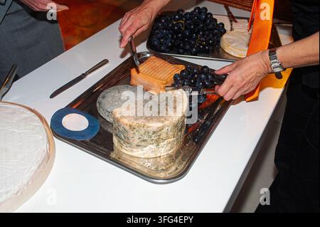Gäste servieren gereifte und weiche Käsesorten mit frischen Trauben von einem Silbertablett an einem Buffet, wobei sie Messer und Zangen verwenden, um Vorspeisen während eines Cas zu auswählen Stockfoto