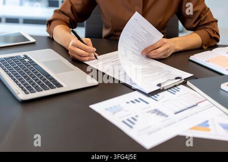 Geschäftsfrau überprüft die Bedingungen eines Rechtsvertrags, während sie offizielle Unterlagen unterzeichnet und mit Laptop und Finanzberichten an einem Schreibtisch im Büro arbeitet Stockfoto
