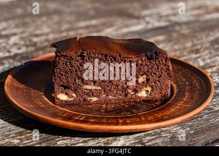 Scheibe hausgemachter Schokoladenspongekuchen auf Tonplatte. Köstliches Stück dunkler Schokoladenbrownie oder Kekskuchen mit Füllung aus Obst, serviert auf rustikalem Ton Stockfoto