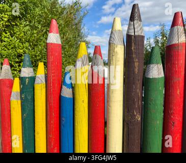 Kreative Farbstifte, die wie ein Zaun im Gartenerde angeordnet sind Stockfoto