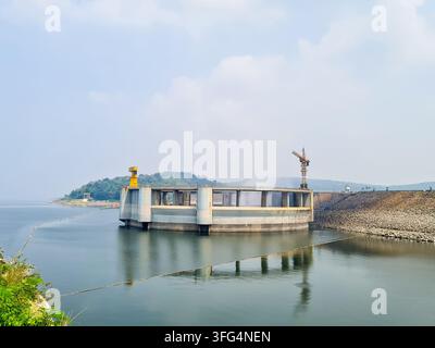 Beton-Einspeiseturm in einem Staudammreservoir mit Stein Damm und Baukran. Anlage für Wassermanagement und Wasserkraftgewinnung Stockfoto
