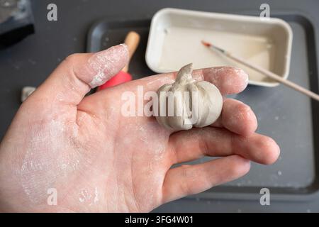 Miniatur-Ton-Kürbis, der in der Handfläche als handgefertigter Herbstschmuck ausgestellt ist Stockfoto