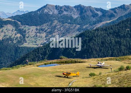 Zwei kleine Flugzeuge, die auf einer grasbewachsenen Fläche in der Nähe von Bergen geparkt sind Stockfoto
