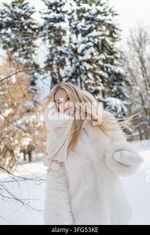 Lächelnde junge Frau wendet sich der Kamera zu, während ihr langes blondes Haar sich in der Winterluft bewegt und ein frisches saisonales Schönheits- und Moden-Lifestyle-Porträt erzeugt Stockfoto