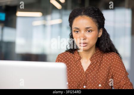 Junge biracial Businessfrau, die sich intensiv an ihrem Schreibtisch in einem modernen Büro konzentriert, an einem Laptop arbeitet und berufliche Aufgaben mit Hingabe und Konzentration verwaltet Stockfoto