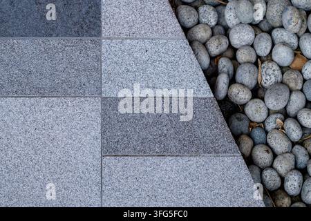 Hochwinklige Nahaufnahme von grauen Granitsteinfliesen, gepaart mit dekorativen grauen Flusskieseln in einem modernen Außengartenweg Stockfoto