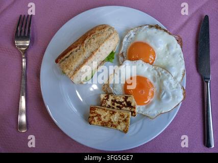 Eine Ansicht von oben eines klassischen Frühstücks, das auf einem weißen Teller serviert wird, der auf einer lila Tischdecke liegt. Der Teller enthält zwei Spiegeleier Stockfoto