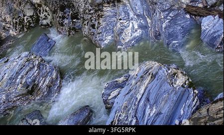 Hochwinkelaufnahme eines kalten Bergbachs, der sich durch gestreifte Blauschiefer- und Marmorformationen in den Alpen in Österreich schneidet Stockfoto