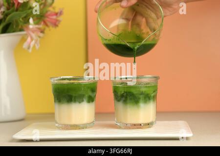 Frauenhand gießt Matcha in das Glas, Prozess der Herstellung von Matcha-Grünteee-Latte Stockfoto