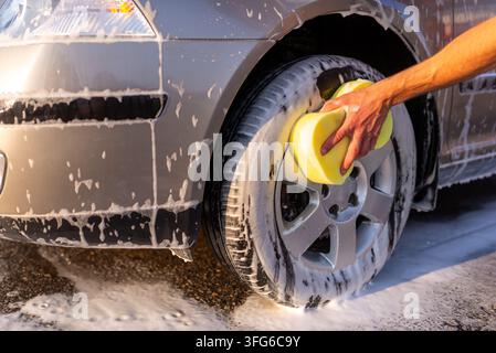 Mann wäscht Radlegierung mit gelbem Schwamm Stockfoto