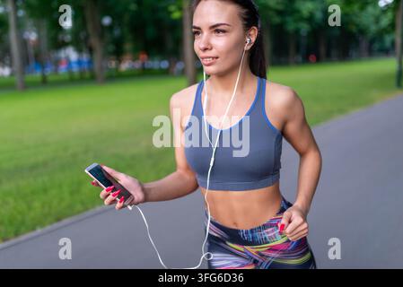 Junge sportliche Frau läuft auf einem Parkweg mit einem Smartphone Stockfoto