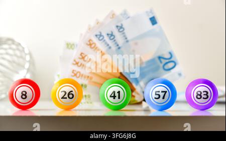 Fünf farbenfrohe nummerierte Lotteriekugeln stehen in einer Reihe vor verschwommenen Euro-Banknoten und vereinen Symbole für Glücksspiel, Glück, Geld und Gewinn. Stockfoto