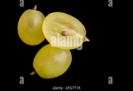 Frische grüne Trauben mit einer halbierten Traube, die das durchscheinende Fleisch und den Kern zeigt, isoliert vor schwarzem Hintergrund. Stockfoto