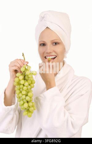 Junge blonde Frau in weißem Bademantel, Ausschnitt isst Trauben, Studionaufnahme, Bundesrepublik Deutschland Stockfoto