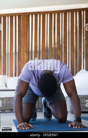 Mittlerer erwachsener afroamerikanischer Mann kniet und streckt sich auf blauer Matte im Wohnbereich Stockfoto