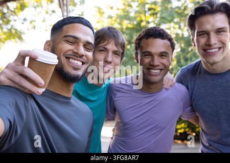 Verschiedene männliche Freunde, die zusammen im Park posieren und lehnen und einen Takeaway-Kaffeebecher halten Stockfoto