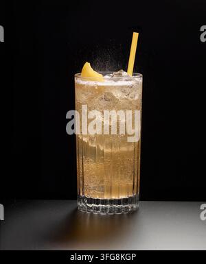 Rosa funkelnder Cocktail in einem Longdrinkglas auf Eiswürfeln vor schwarzem Hintergrund, Zitronenschale als Garnitur, Studioaufnahme Stockfoto