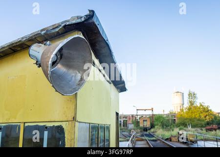 Nahaufnahme eines großen Metall-Scheinwerfers an einer verrosteten gelben Lokomotivkabine in einem alten Bahndepot in Dej, Rumänien, mit verlassenen Zugwagen und einem Wasser Stockfoto