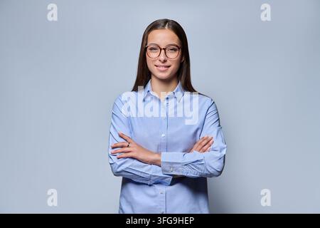 Junge Frau mit Brille lächelt in die Kamera vor hellem Hintergrund Stockfoto