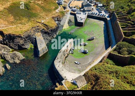 Fischerboote, die auf dem Gezeitenmuddel im Hafen von Porthgain, Pembrokeshire, aufliegen, Steinmolare und Küstenklippen umgeben die historische Einfahrt im Sommer Stockfoto