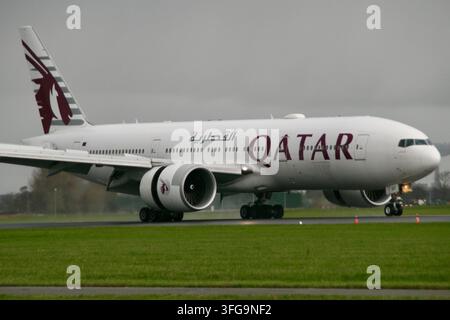 Ein Qatar Airways Boeing 777 Passagierflugzeug taxiert mit Umkehrschub auf einer nassen Landebahn unter bewölktem Himmel nach der Landung. Stockfoto