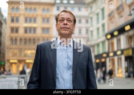 Ein mittelalter Geschäftsmann steht in einer verschwommenen Stadtstraße und schaut nachdenklich nach oben. Stockfoto