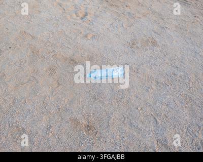 Verlassene leere klare Plastikwasserflasche, die auf sandigem Kiesboden liegen gelassen wurde, betont Umweltmüll und Plastikverschmutzung. Stockfoto