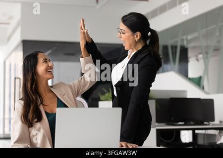 Vielfältige Geschäftsfrauen, die sich im Büro bei einem High-Five feiern, um den Erfolg der Zusammenarbeit Stockfoto