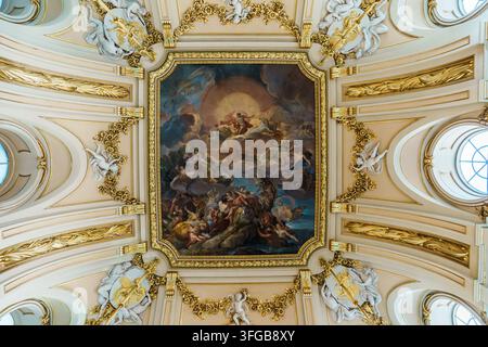 Madrid, Spanien: 7. Apr. 2025 – Ein lebendig gemaltes barockes Deckenfresko, das mythologische Figuren und Wolken darstellt, ist von kunstvollem goldenen Stuck umrahmt und ch Stockfoto